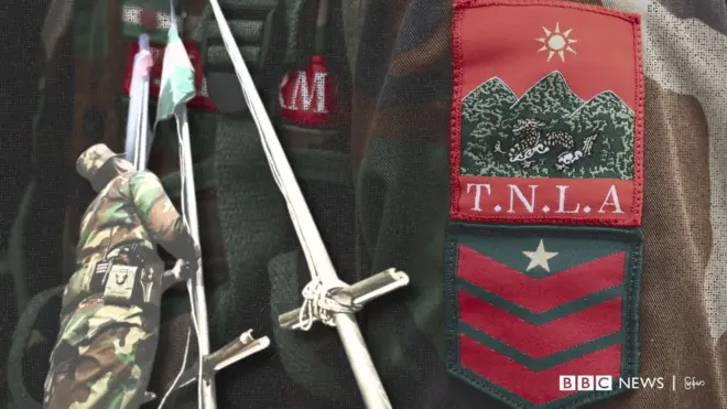 အလံတင်နေတဲ့TNLAတပ်ဖွဲ့ဝင်တစ်ဦးနဲ့ TNLAယူနီဖောင်း ‌ဘတ်တံဆိပ်