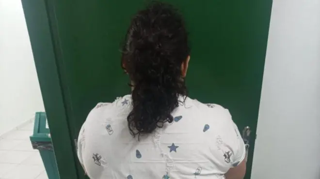 Mujer arrestada, de espaldas frente a una puerta verde