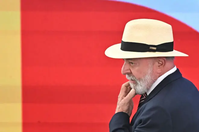Lula aparece de perfil, usando chapéu, em fundo vermelho
