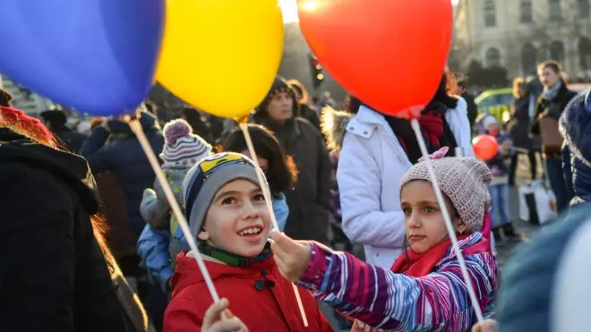 Children hold balloons in the colours of the Romanian flag as people protest in front of the government headquarters against the government's contentious corruption decree in Bucharest, Romania on 5 February 2017
