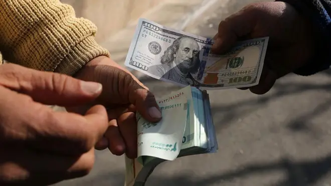 دستان دو نفر در حال معامله با اسکناس دلار آمریکا و ریال ایران