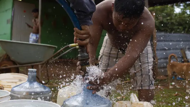 Joven llena garrafas de agua de manguera de camión cisterna