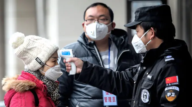 Security personnel check the temperature of passengers in the Wharf at the Yangtze River in Wuhan, Hubei province