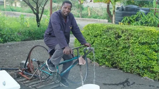 Bernard Kiwia outside ontop bicycle wey dey run water-pump