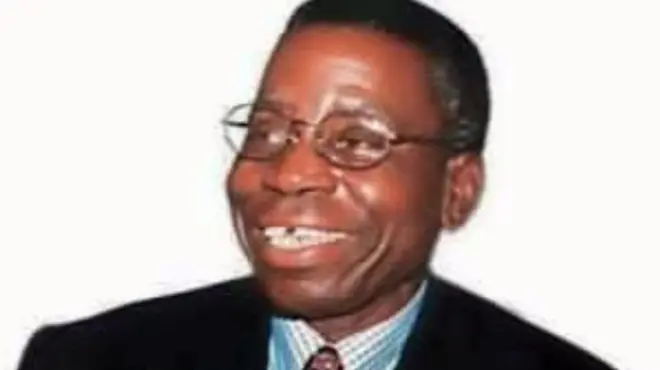 Oloye Bola Ige wọ kóòtù aláwọ̀ dúdú àti Táì. Ó ń rẹrìn pẹ̀lú eji laarin eyin rẹ, to si gbe igo soju