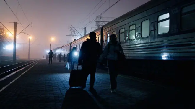 ウクライナ東部ドンバス地方から逃れる人々。ロシア軍のドローンに狙われないよう霧かかかる中、列車のそばをスーツケースを引いて歩いている