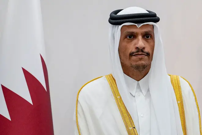 أرشيفية لرئيس الوزراء ووزير الخارجية القطري، الشيخ محمد بن عبد الرحمن آل ثاني بلباس تقليدي يغلب عليه اللون الأبيض وخلفه العلم القطري.