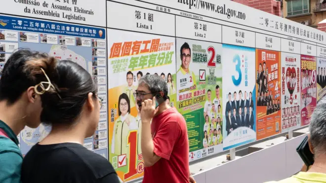 一名穿紅色上衣的男子在澳門立法會選舉候選組別展示板前經過。