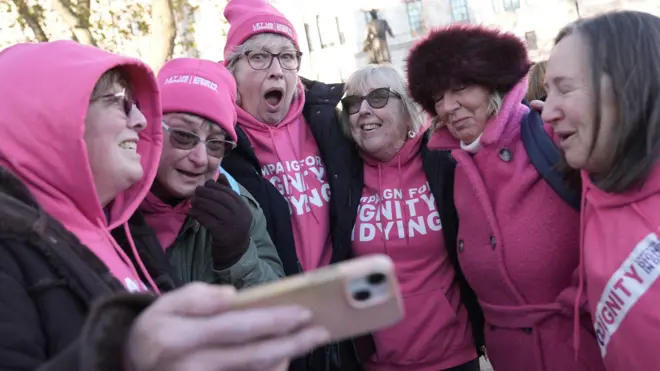 Шесть женщин в розовых худи со слоганами в поддержку закона об эвтаназии делают радостное селфи.