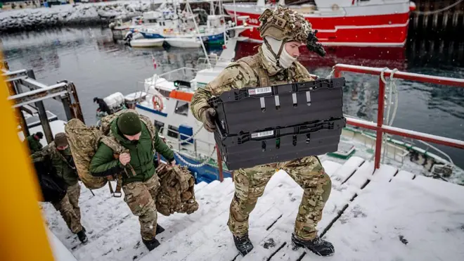 Danimarkalı askerler ellerinde askeri çanta ve kutularla deniz kenarındaki bir merdivenden çıkıyor. 