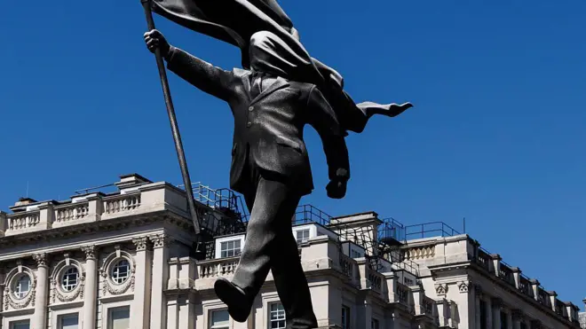 Una estatua que representa a una persona descendiendo de un pedestal con el rostro cubierto por una bandera ondeante en Waterloo Place, el 30 de abril de 2026, en Londres, Inglaterra.