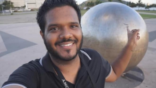 Eduardo Dias sorri apontando para escultura em forma de bola