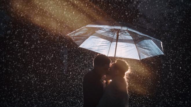 Casal se beija sob chuva e debaixo de guarda-chuve