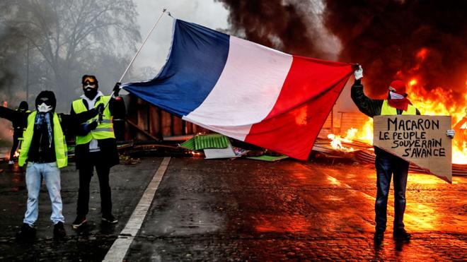 Protesters hold a French flag near a burning barricade during a protest of Yellow vests