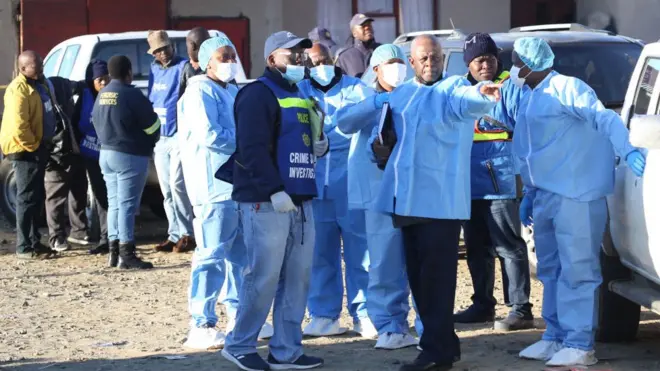 رجال الشرطة والمحققون يرتدون ملابس واقية قبل الدخول إلى حانة في بلدة شرق لندن بجنوب إفريقيا