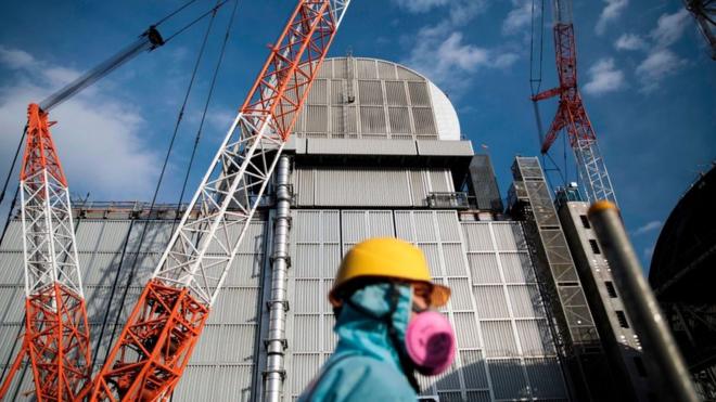 An employee of Tokyo Electric Power Company (TEPCO) walks past the company's reactor number 3 at Fukushima Dai-ichi nuclear power plant