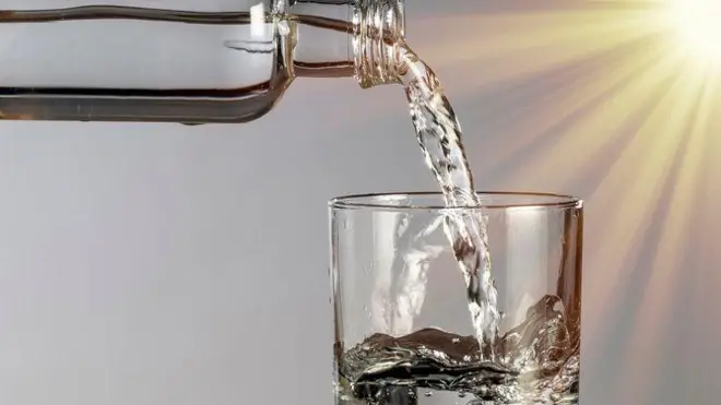 Скляна пляшка з природною водою на сірому тлі, освітлена променем сонця - стокове фото