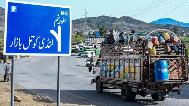 یک موتر باربری در حال عبور از لوحه کنار سرک که روی آن مسیر تورخم و لندی کوتل بازار نوشته شده است.