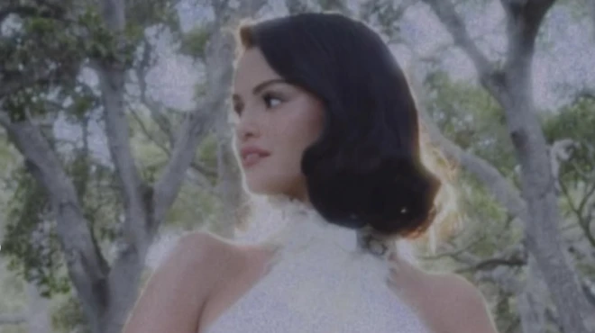 Selena Gomez, a young woman with dark hair, looks to the side as she poses in front of trees while wearing a while wedding dress.