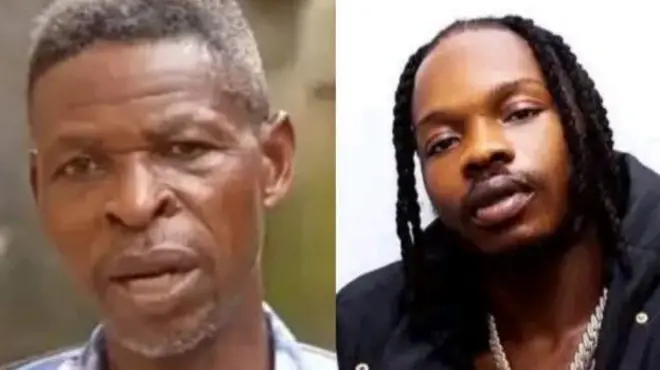 Baba Mohbad àti Naira Marley duro papọ, baba Mohbad wọ aṣọ aláwọ̀ búlúù nigbati Naira Marley wọ aṣọ dúdú, tó sì di irun rẹ.