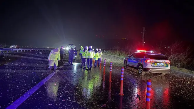 Sarı ceketler giymiş polisler, kazanın yaşandığı yoldaki parçalara bakıyor. Otoyol çok geniş ve karanlık.