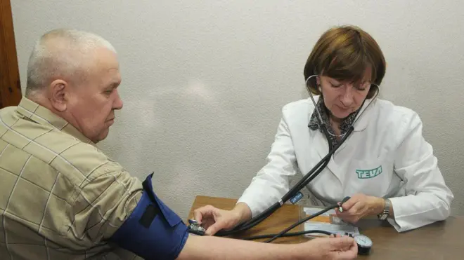 Лікар в білому халаті вимріює тиск пацієнту у картатій сорочці 