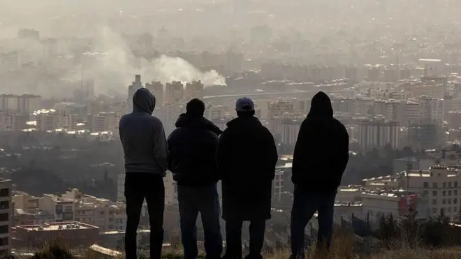 जंग शुरू होने के तीन दिन बाद सोमवार को तेहरान में उठते धुंए को देखते लोग