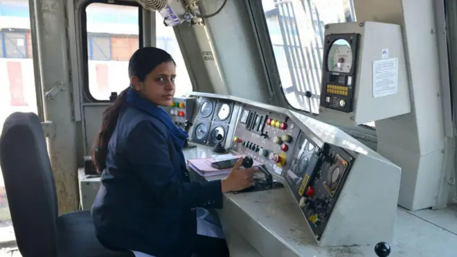 නිල් පැහැ නිල ඇඳුමක් ඇඳ දුම්රිය ධාවනයට සූදානම්ව සිටින ඉන්දියානු කාන්තා දුම්රිය රියදුරුවරියක් 