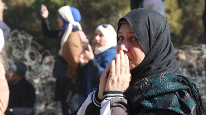 Una mujer con las manos juntas mira a la cámara mientras espera cerca de la prisión de Saydnaya, en Siria