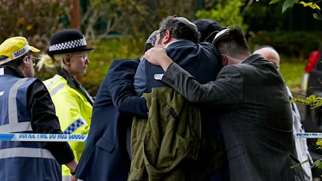 Członkowie społeczności żydowskiej pocieszają się nawzajem w pobliżu synagogi Heaton Park Hebrew Congregation w Crumpsall w Manchesterze
