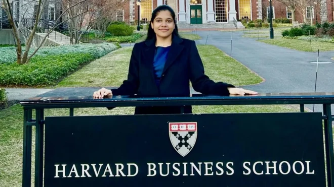 شریا میشرا پشت تابلوی مدرسه تجارت هاروارد ایستاده