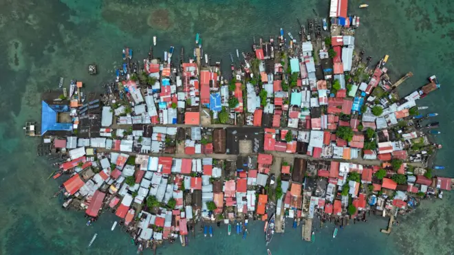 Aerial photo showing the island of Gardi Sugdub, a cluster of densely-packed red and grey roofs with boats, jetties and buildings sticking out into the surrounding ocean in all directions