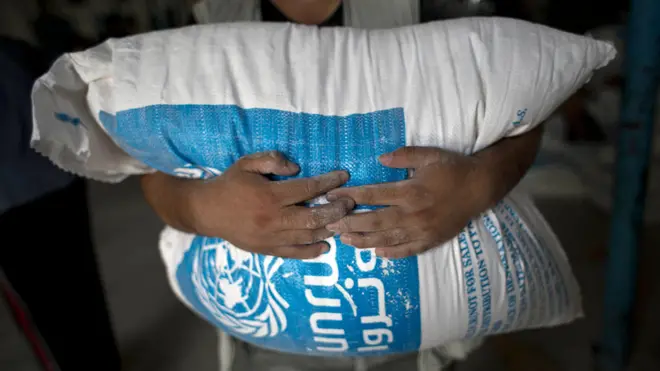 یک مرد فلسطینی کیسه‌ای آرد گندم را حمل می‌کند که در مرکز توزیع کمک‌های آژانس امداد و کار سازمان ملل در رفح در جنوب نوار غزه توزیع شده است.