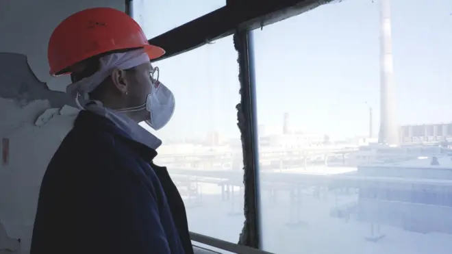 Hombre con ropa de protección mira por una ventana donde se ve la planta nuclear de Chernobyl