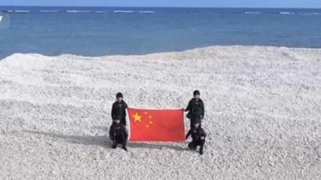 四名身穿黑衣的海警在北京聲稱擁有主權的爭議沙洲上展示中國國旗