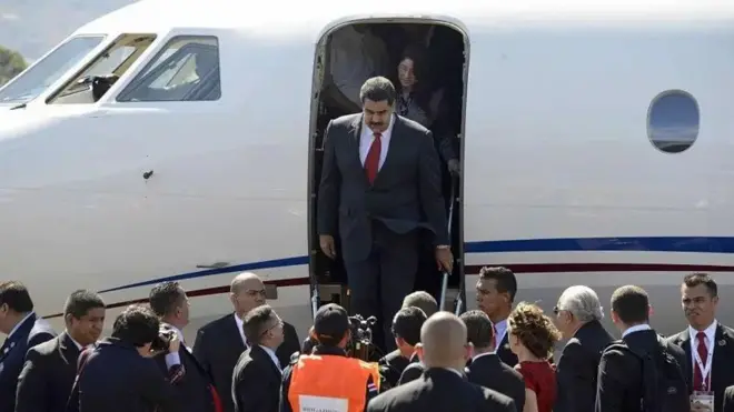 A foto mostra Maduro, um homemaposta fifa betanopele clara, cabelo e bigode pretos, vestindo um terno escuro sobre camisa branca e gravata vermelha, descendo da escadaaposta fifa betanoum avião. 