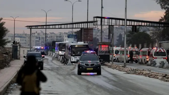 Çakarlı bir araç önde arkadan otobüsler geliyor. Geniş yolun sağında ambülanslar park etmiş. 