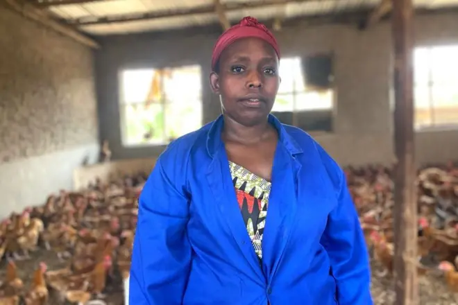 Clémence Murekatete yambaye itaburiya y'ubururu ahagaze mu nzu y'inkoko ze