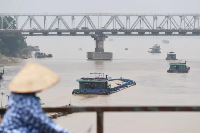 Một người phụ nữ đội nón lá đi trên cây cầu bắc qua sông Hồng 