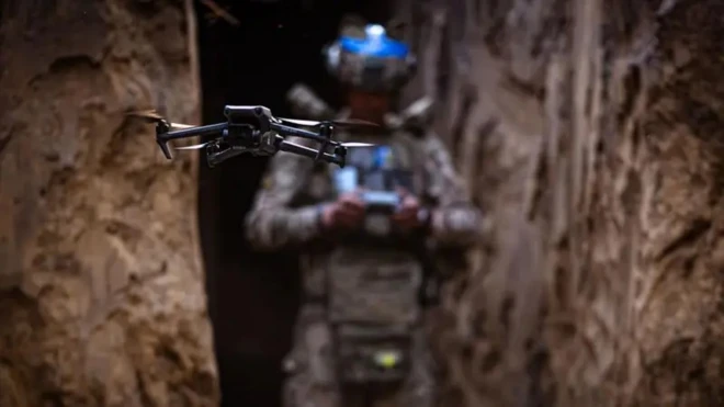 На переднем плане дрон, на заднем, размытом, упарвляющий им военный.