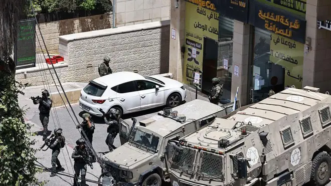 جنود إسرائيليون يرفعون أسلحتهم أمام محل صرافة خلال مداهمة في رام الله بالضفة الغربية المحتلة في 27 مايو/أيار 2025.