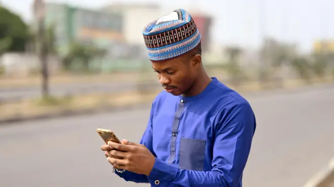 One man wey wear blue native dress hold phone