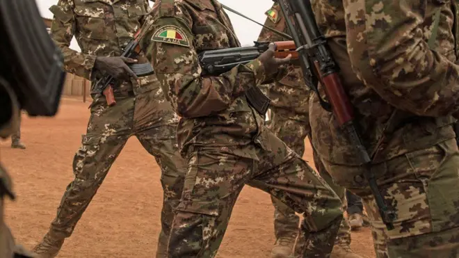 Des soldats maliens en tenue de camouflage brandissent des armes.