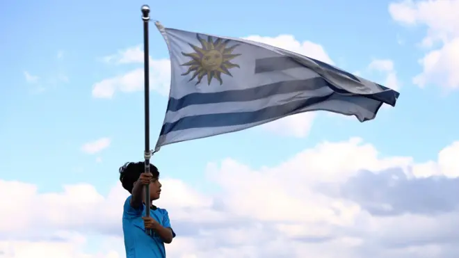 Un niño agita la bandera de Uruguay con un cielo celeste de fondo.