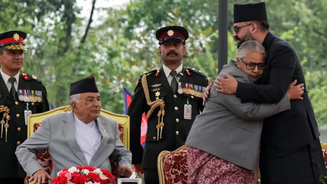 मेचमा बसेका राष्ट्रपति र बालेन शाहसँग अङ्कमाल गर्दै सुशीला कार्की। पछाडि उभिरहेका सैनिक सुरक्षाकर्मीहरू