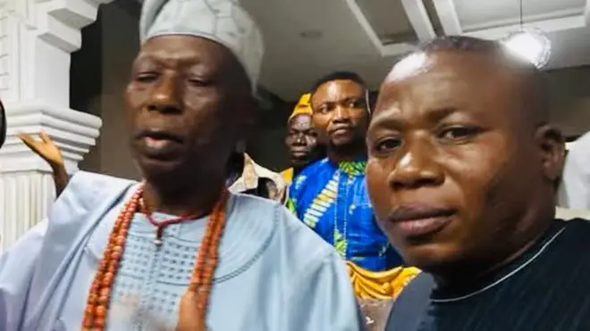 Sunday Igboho to wọ aṣọ aláwọ̀ omi aro, dúró sí apa ọtun Eleruwa, Ọba Samuel Akindele, to wọ agbada búlúù àti ìlẹ̀kẹ̀ lọrun tí Agbẹnusọ fún Sunday Igboho, Koiki, to wọ aṣọ aláwọ̀ pinki àti fìlà, dúró sí apá àlàáfíà Eleruwa 