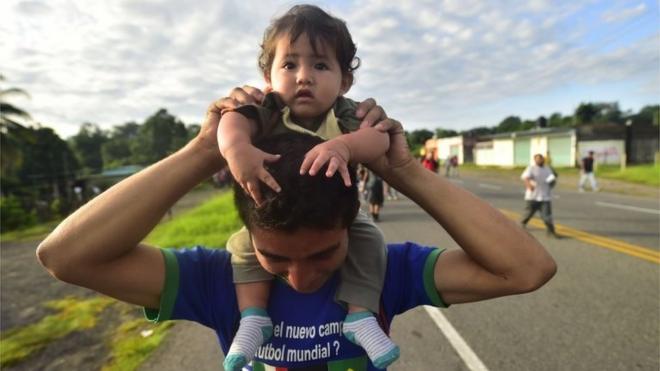 A Honduran migrant holds a baby as he takes part in a caravan heading to the US on October 21, 2018.