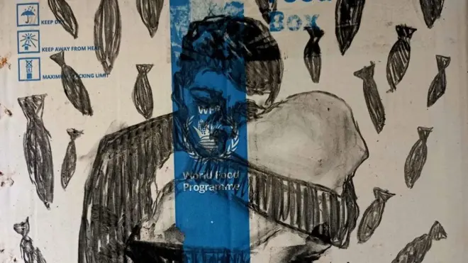 بالأبيض والأسود رسم لأب يحتضن ابنه الرضيع، تتساقط عليهم الصواريخ على لوحة المساعدات.