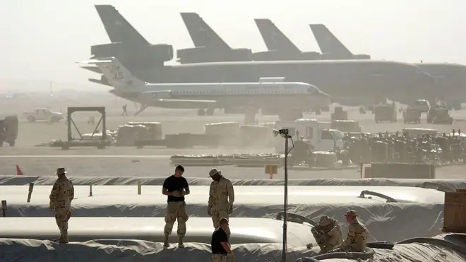 Önde askeri personal yükseltiler üzerinde geride uçaklar sislerin ardından görünüyor. 