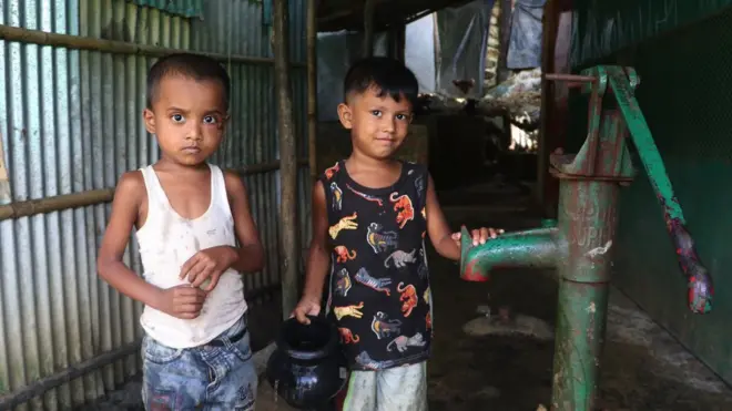 Children fill a black jug with water in Cox's Bazar, Bangladesh on 9 July, 2022. More than a million Rohingya Muslims, who were displaced due to the long-standing oppression in Myanmar, continue to live in the makeshift camps with little access to basic needs.